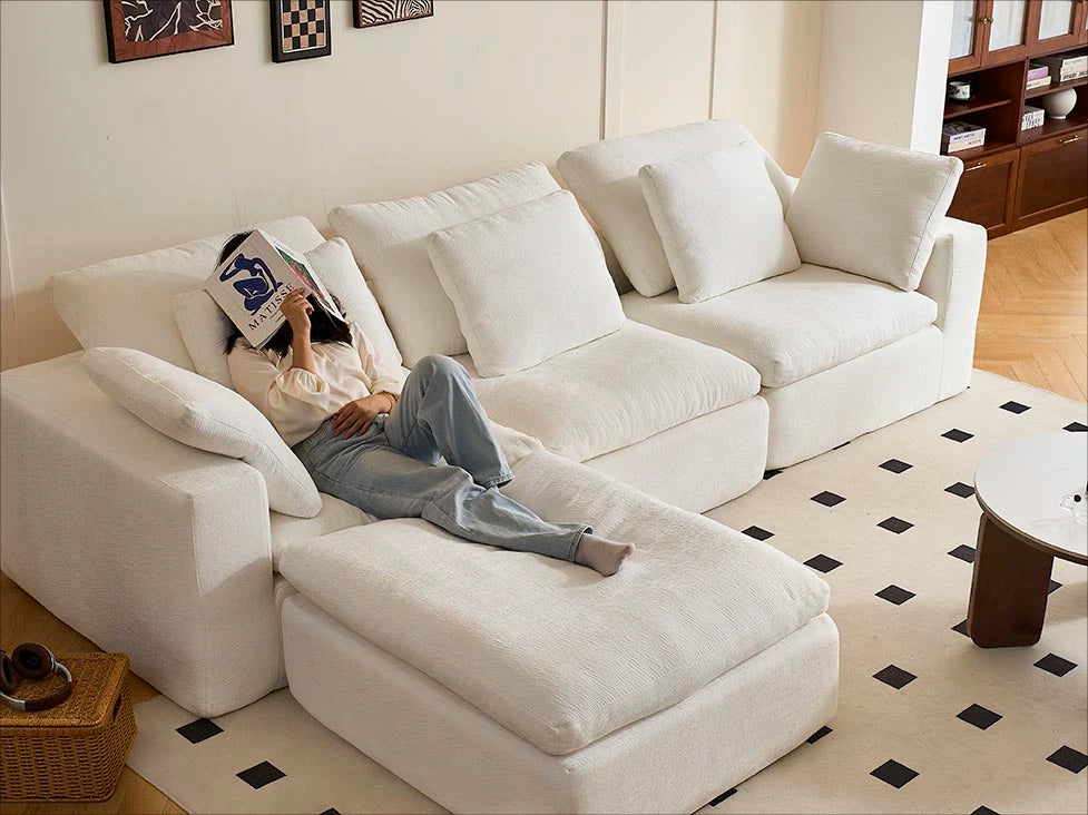 A woman lazes with a book in hand on the modular white 4-seater L-shaped sofa from Cozy Nest.