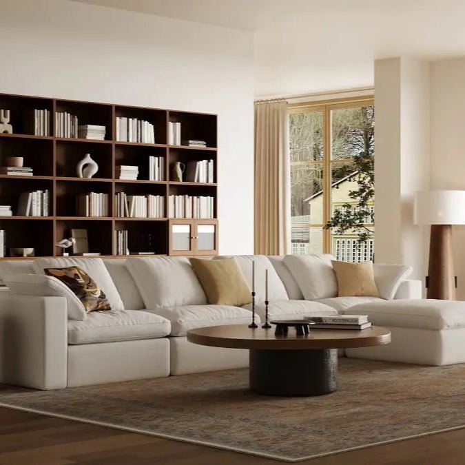 In the simple living room, there is a 5-seater modular white sofa and a whole wall of modular walnut-colored bookcases.