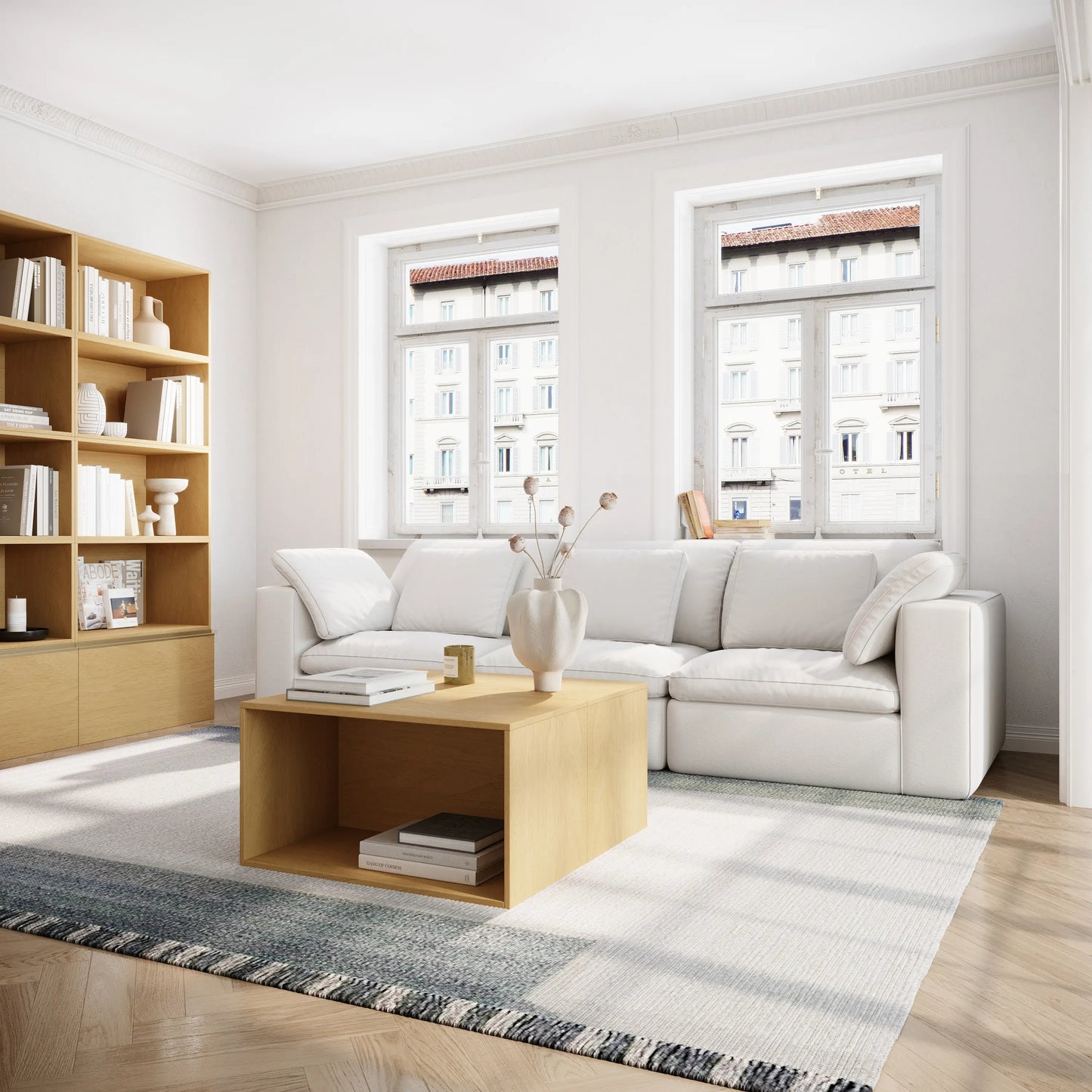 The bright living room is furnished with a three-seater white modular sofa and a coffee table and bookcase consisting of a log-colored modular basic cabinet.