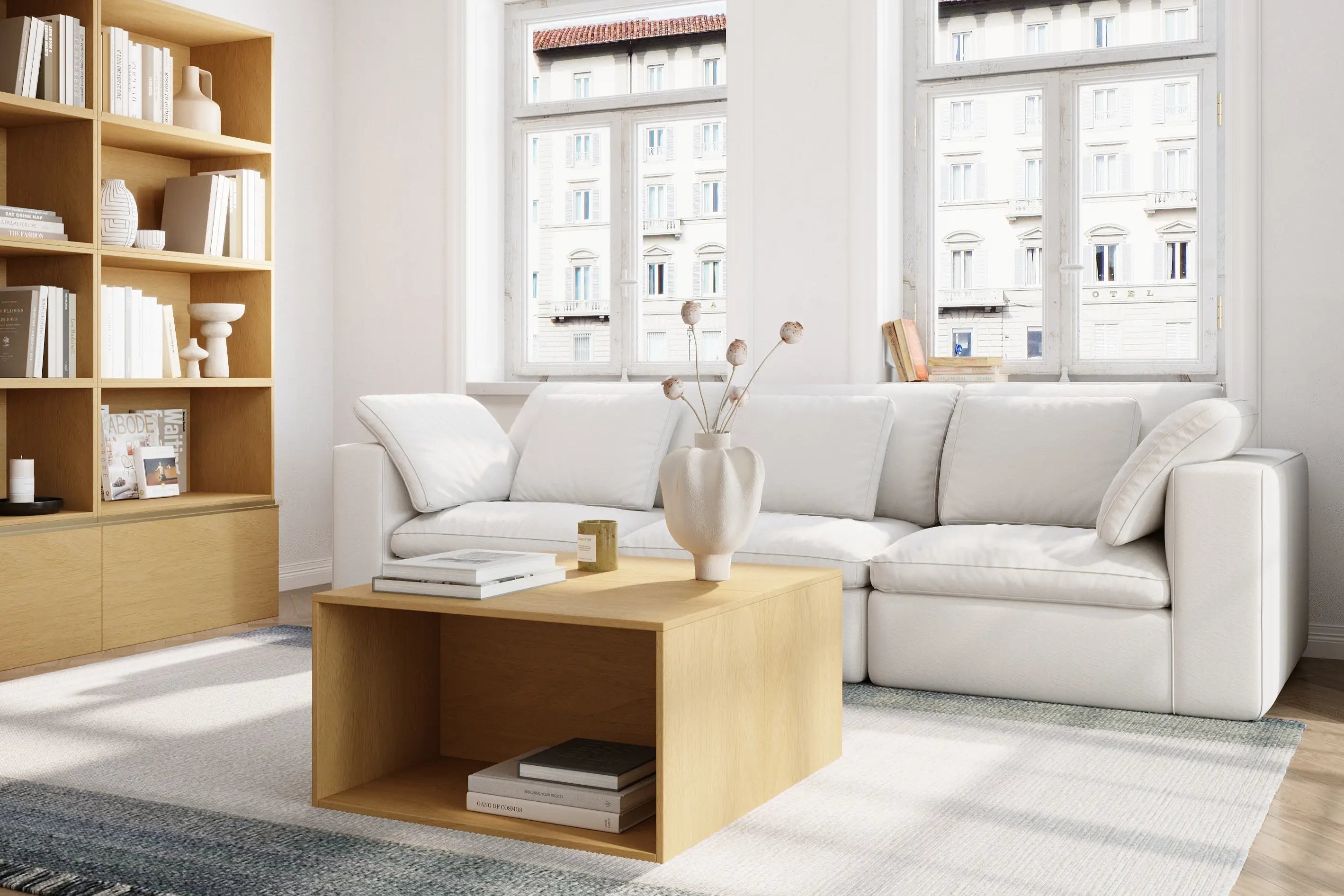 The bright living room is furnished with a three-seater white modular sofa and a coffee table and bookcase consisting of a log-colored modular basic cabinet.
